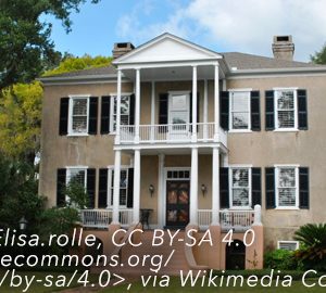 The Significance of Tabby Manse. Large house with black shutters and 2 story porch with columns and elevated on red steps