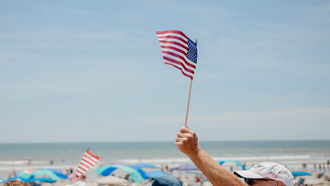 4th of July Events. salute from the shore. A man waving a small American Flag on the beach